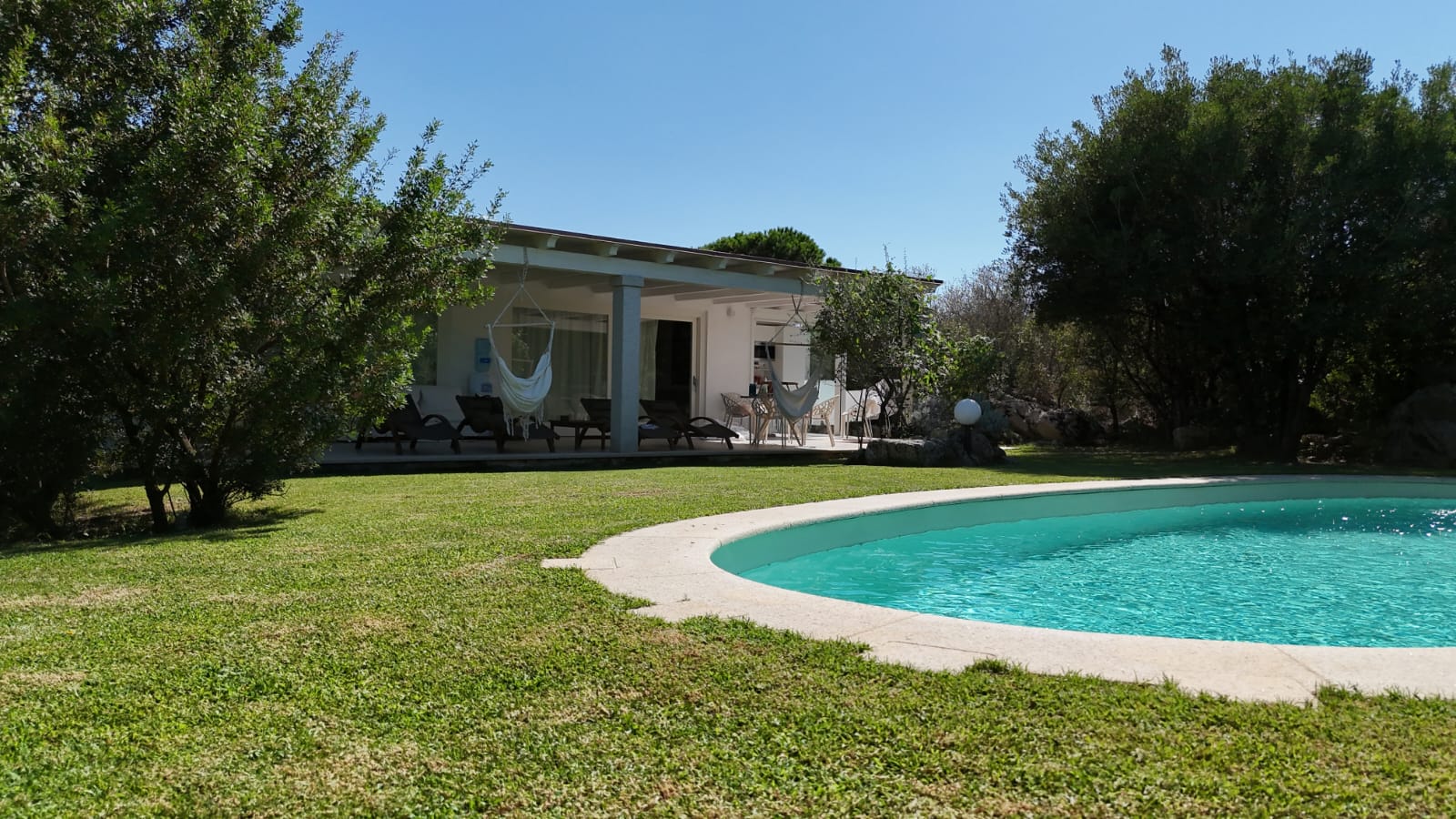 La piscina e il portico con le sedie-amaca, visti dal prato